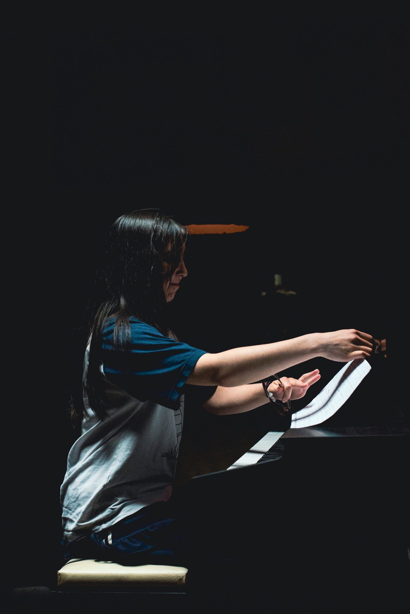 Leerling speelt piano in een spot op een donker podium